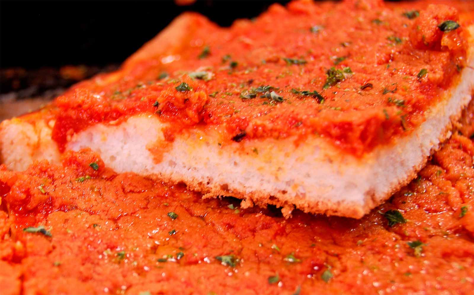 close up of a sicilian pizza slice covered in red sauce