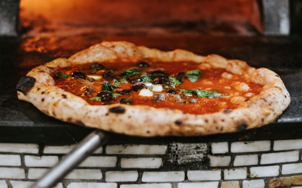 marinara pizza on a pizza peel in a pizza oven
