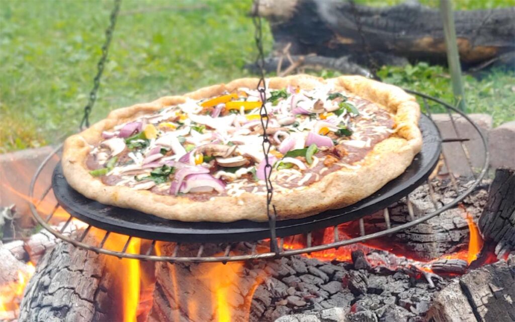 campfire pizza cooking on a hanging tripod stone