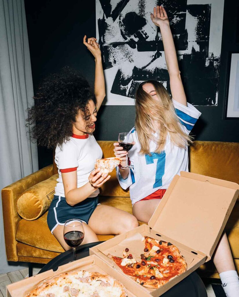 two girl pizza snobs drinking wine over some boxes of pizza