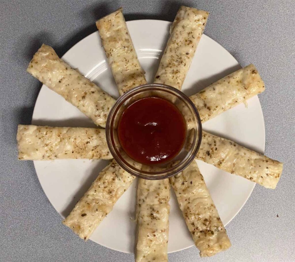plated homemade breadsticks in a circle with small cup of red dipping sauce in the middle