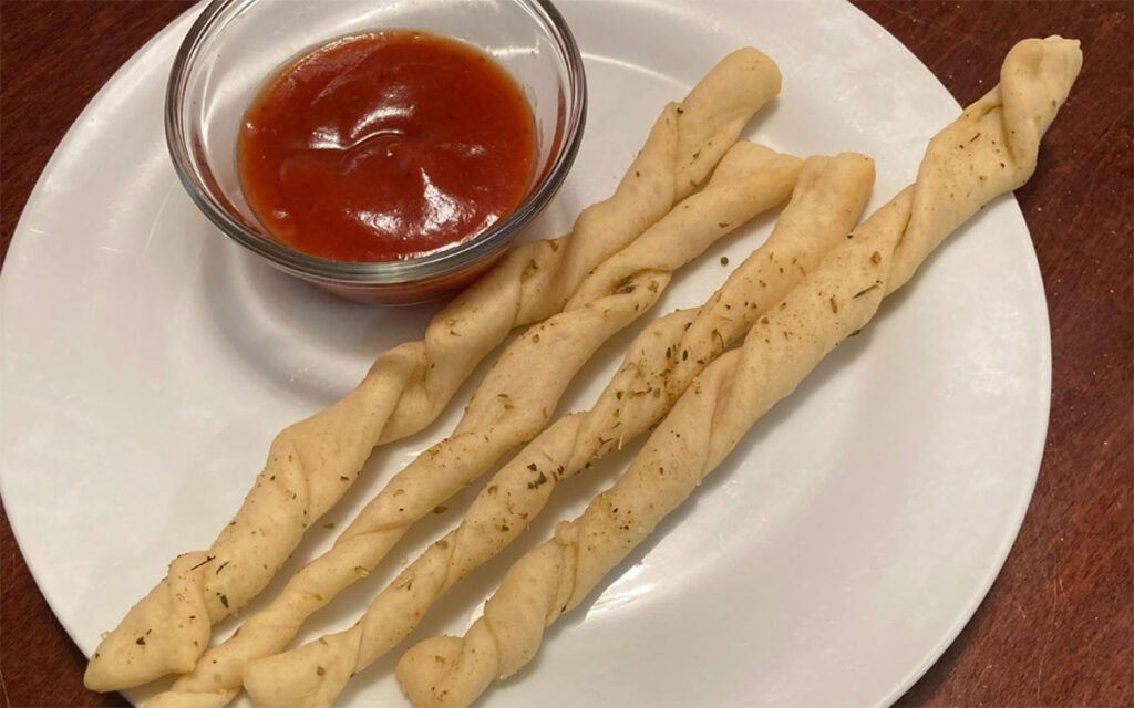 classic thin breadsticks on a white plate with small cup of red sauce